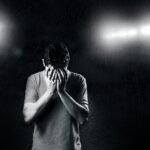 Black and white photo of a man covering his face, conveying emotion and solitude.